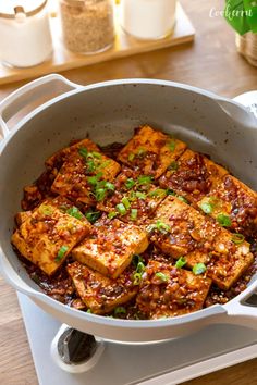 tofu is in a pan on top of the stove with green onions and seasoning