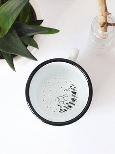 a black and white coffee cup sitting on top of a table next to a plant