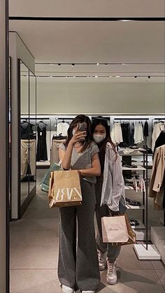 two women standing in front of a store holding shopping bags and talking on the phone