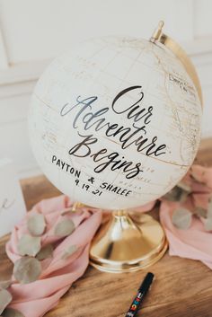 a globe with writing on it sitting on top of a wooden table next to a pen