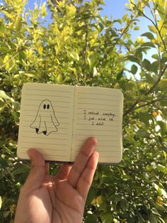 someone holding an open notebook with a drawing of a ghost on it in front of some trees