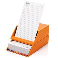 an orange desk organizer with a notepad and pen in it, on a white background