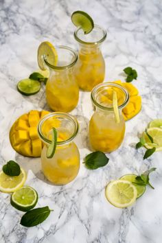 three mason jars filled with lemonade and limes on a marble counter top next to sliced mangoes