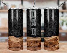 two black and white tumblers with the word dad printed on them sitting on a wooden table