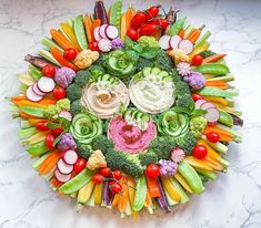 an arrangement of vegetables arranged in a circle on a marble counter top, with the center surrounded by smaller veggies