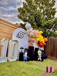 an outdoor birthday party with balloons and anime characters on the lawn, in front of a fence