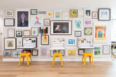 two yellow stools are in front of a wall full of framed pictures and artwork