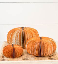 three pumpkins made out of wicker sitting on a wooden board with white wall in the background