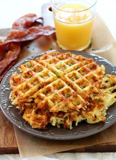 a plate topped with waffles and bacon next to a glass of orange juice