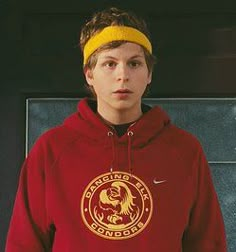 a young boy wearing a red hoodie and yellow headband standing in front of a wall