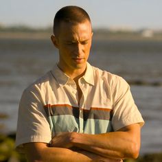 a man with his arms crossed standing in front of the water and looking at something