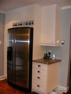 a stainless steel refrigerator in a kitchen with white cabinets and wood flooring next to a trash can