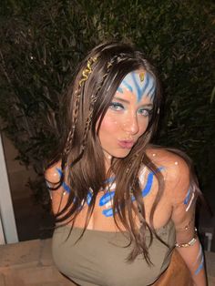 a woman with blue paint on her face and body is posing in front of a tree