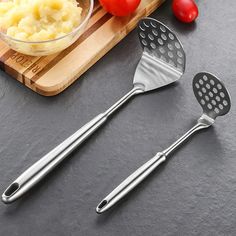 two kitchen utensils on a cutting board with tomatoes and mashed potatoes