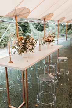 a long table with clear stools and flowers on it in the middle of an outdoor tent