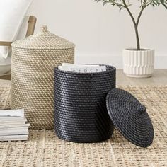 three black baskets sitting on top of a rug next to a vase and planter