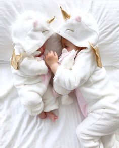 a baby wrapped in a unicorn costume laying on top of a white bed covered in blankets