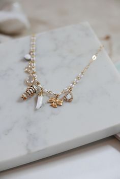 Meet your new favorite charm necklace -- a whimsical mix of lucky gold-toned charms on an enameled white/ gold-filled chain. Dainty yet bold, serious yet trendy and fun; guaranteed to get you compliments. 7 charms to bring you the most luck: Enameled white bead (from our fringe chokers!) tiny gold plated star with 3 CZ crystals Clear Quartz set in a vermeil twisted rope setting, tear drop shaped Vintage cloisonné wiggle fish in center Lucky enameled white horn - for protection Vintage brass bow Whimsical White Jewelry With Pearl Charm, Dainty Gold Plated Charm Necklace For Good Luck, Gold Plated White Necklaces With Charms, Gold Plated White Necklace With Charms, White Gold Plated Charm Necklace With Adjustable Chain, White Gold-plated Charm Necklaces, White Gold Plated Necklaces With Charms, White Gold-plated Charm Necklace With Adjustable Chain, White Gold Plated Necklace With Charms