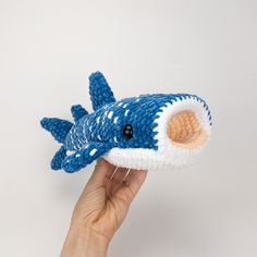 a hand is holding a blue and white knitted toy that looks like a shark