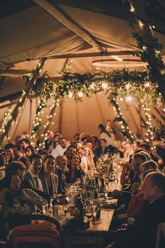 a group of people sitting around a table in a tent with lights on the ceiling