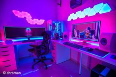 a computer desk with two monitors and a keyboard on it in a room that has purple lighting