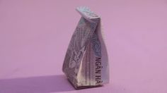 an origami money bag sitting on top of a pink surface with purple background