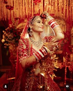 a woman in a red and gold bridal outfit is holding her hands up to her head