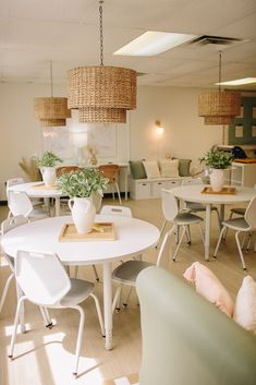 a room filled with white tables and chairs next to green couches on top of hard wood flooring