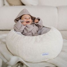 a baby is sitting in a bean bag on the floor wearing a hoodie and smiling