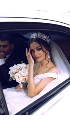 a woman in a wedding dress sitting in a car with her hand up to her face