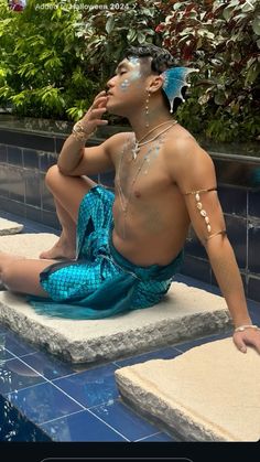 a man sitting on the edge of a pool with his face painted like a butterfly