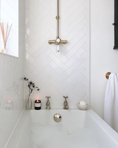 a white bathroom with herringbone tile and gold faucet, along with candles