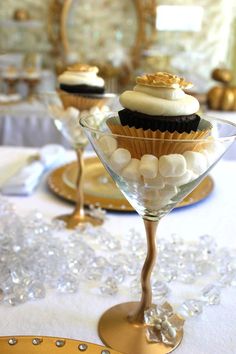 cupcakes are sitting in small glasses on a white tablecloth with gold trim