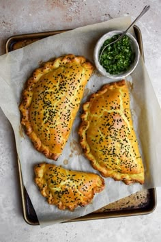 three pieces of chicken sitting on top of a baking sheet next to a bowl of pesto