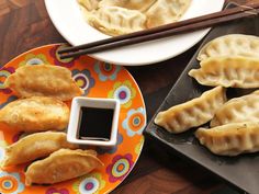 two plates with dumplings and dipping sauce next to chopsticks on a table