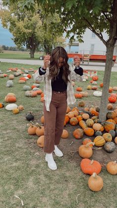 a woman standing next to a tree surrounded by pumpkins