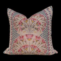 a pink and blue pillow with flowers on the front, sitting on a black background