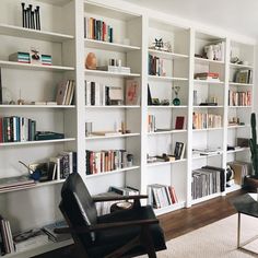 an instagram photo of a living room with white bookcases and black leather chair