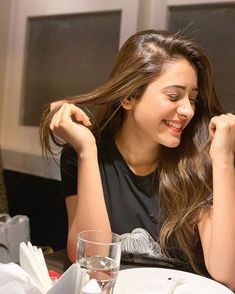 a woman sitting at a table smiling and holding her hair