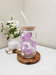 a glass jar with a straw in it sitting on a table next to a flower vase