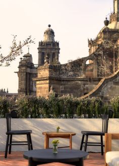 two chairs and a table on a brick patio with an old building in the background