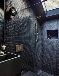 a black tiled bathroom with a skylight above the sink and shower head on the wall