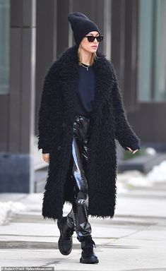 a woman in black coat and leggings walking down the street with her hand on her hip