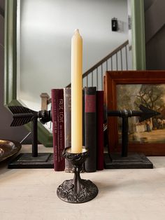 a candle is sitting on a table next to some books and a framed painting in the background