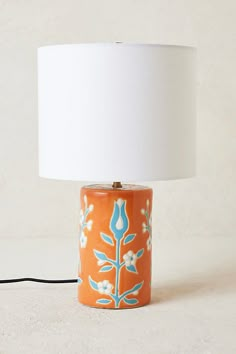 an orange and blue table lamp with a white shade on the top, sitting next to a black cord