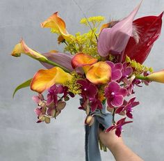 a person holding a bouquet of flowers in front of a gray wall with white writing on it