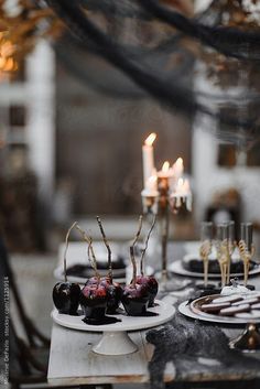 the table is set with black and white plates, silverware, candles and desserts