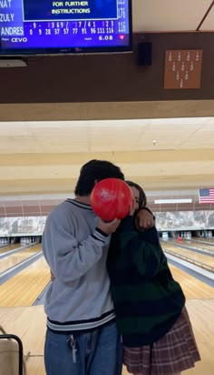 two people hugging each other in front of a bowling alley with red balls on the floor