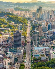 an aerial view of a city with tall buildings and trees in the foreground, surrounded by mountains