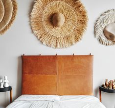 a bed with white sheets and two straw hats on the wall above it's headboard